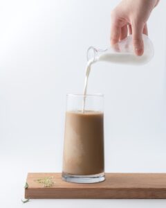 person pouring milk into chocolate filled glass cup